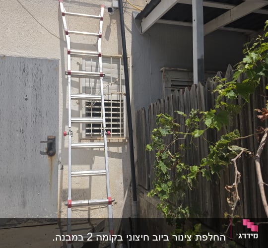 סולם ליד קיר חיצוני עם צינור וגדר עץ